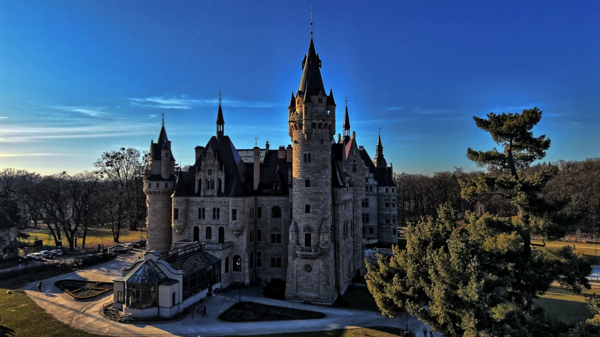 Zamek w Mosznej – widok na bajkową rezydencję z licznymi wieżami otoczoną parkiem
