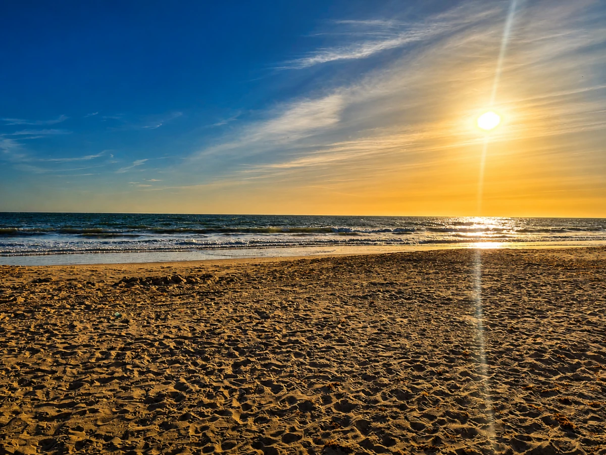 Plaża Playa de la Victoria w Kadyksie o zachodzie słońca, z szerokim pasem piasku, falami Atlantyku i ciepłym światłem nad horyzontem