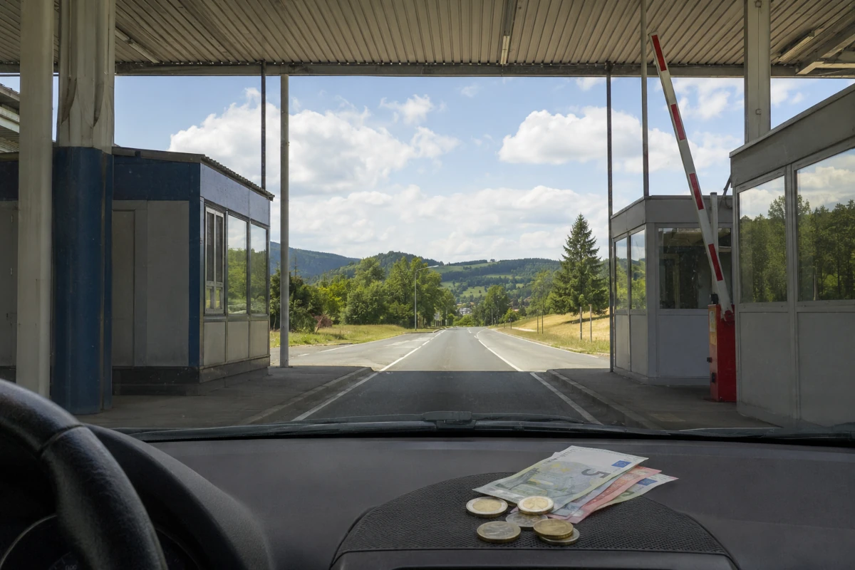 Widok z samochodu na otwarte dawne przejście graniczne w Europie oraz banknoty i monety euro leżące na desce rozdzielczej